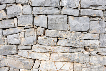 Rugged Gray Stone Wall Of Stacked Rocks With Sparse Dry Grass Detailing
