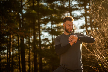 Smiling sportsman checking performance on smartwatch during training in forest
