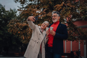 Senior couple taking selfie while enjoying coffee outdoors in autumn