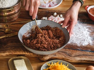 Preparing Cozonac at home involves mixing ingredients in a bowl with a spoon on a wooden table, surrounded by flour, candied peel, and other items