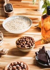 A rustic wooden table displays ingredients like hazelnuts, walnuts, shredded coconut, chocolate, and a liquid flavoring. Everything is ready to start baking a delicious traditional dessert