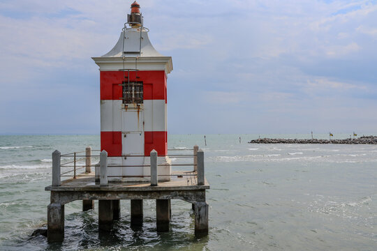 Red and white striped lighthouse on a pier above the sea with cloudy sky
