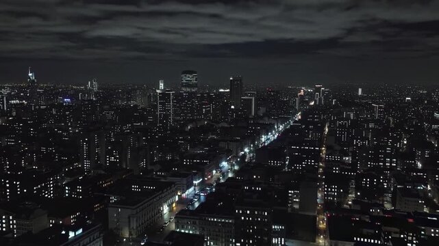 A breathtaking night view of a bustling city is captured from above, with illuminated streets and shimmering skyscrapers. The dark sky and glowing lights highlight the vibrant energy of urban life aft