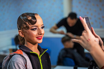 stylist photographs her makeup look on a young dancer before a competition at a salon.