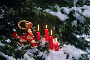 straw Yule Goat and burn candles in winter forest, nature backdrop. Traditional festive decor,...