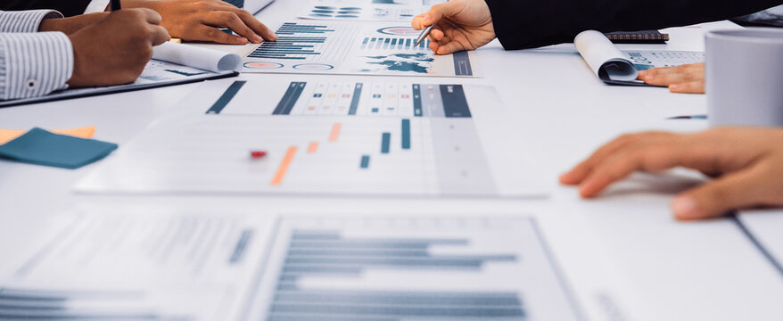 A group of business professionals collaborates during a meeting, analyzing diverse financial charts and reports while utilizing modern technology in a sleek office setting. SACTR - Powered by Adobe