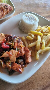 Traditional Fried Fish and Stewed Chicken Served with Coconut Rice, Fried Plantains and Fresh Salad on Wooden Table