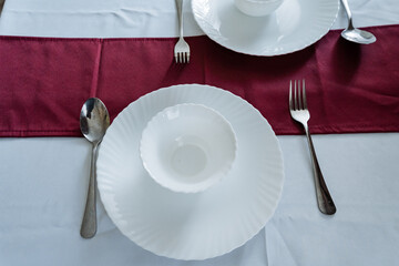 An Elegant Dining Table Setting featuring pristine White Dishware and polished Silverware,...