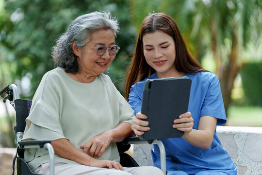 Caring caregiver provides assistance and support to senior in need of care while sharing joyful moment together using tablet outdoors