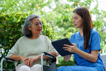 Caring caregiver provides assistance and support to senior in need of care while discussing important information on tablet in serene outdoor setting