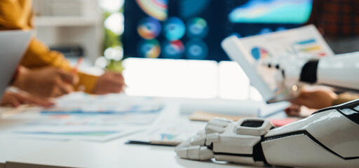 A modern office scene where diverse professionals collaborate on data analysis. A robotic arm is present, highlighting the integration of technology in teamwork.Noogenesis