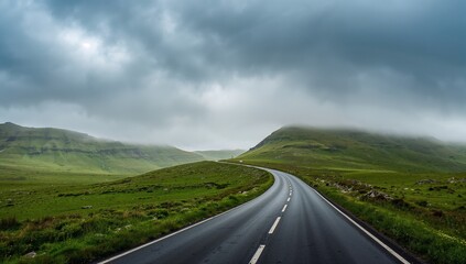 Long winding road cutting through lush green countryside under a moody cloudy sky