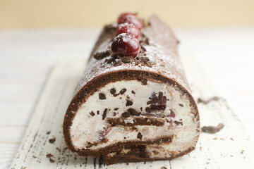 Black Forest roll cake with chocolate and cherries on a white plate. Homemade delicious pastries with delicate cream. Retro recipe concept. Horizontal orientation. Selective focus.