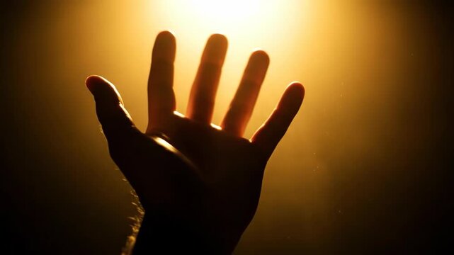 Hand silhouette and outstretched fingers casting warm light and shadow creating dramatic hopeful