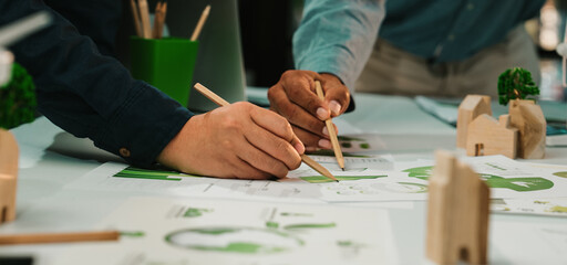 Hands of diverse professionals engaged in collaborative design work, exploring sustainable solutions in a modern workspace filled with innovative sketches and models. SACTR