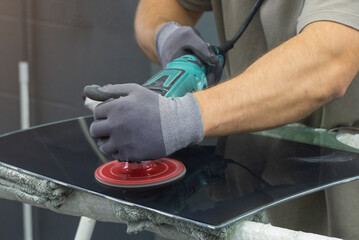 A man polishes the glass of a car with a polishing machine from small scratches with a large one. Auto glass repair, replacement. Car detailing. Hands with an orbital polishing machine. Close-up.