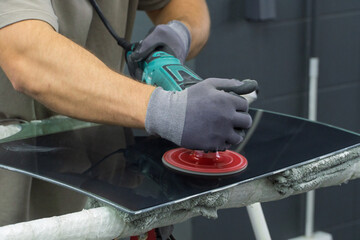 A man polishes the glass of a car with a polishing machine from small scratches with a large one. Auto glass repair, replacement. Car detailing. Hands with an orbital polishing machine. Close-up.