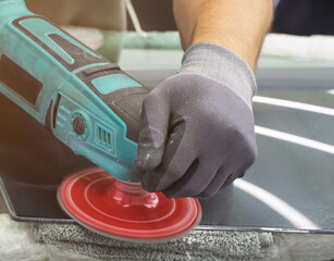 A man polishes the glass of a car with a polishing machine from small scratches with a large one. Auto glass repair, replacement. Car detailing. Hands with an orbital polishing machine. Close-up.