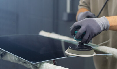 A man polishes the glass of a car with a polishing machine from small scratches with a large one. Auto glass repair, replacement. Car detailing. Hands with an orbital polishing machine. Close-up.