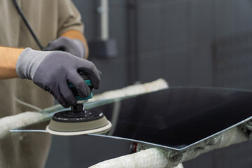 A man polishes the glass of a car with a polishing machine from small scratches with a large one. Auto glass repair, replacement. Car detailing. Hands with an orbital polishing machine. Close-up.