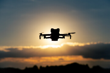 Silhouette of a Drone Flying in the Sky at Sunset with Glowing Sunlight and Scenic Cloudscape in the Background
