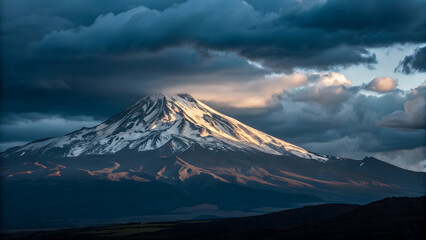 Fototapeta premium Majestic snow capped mountain peak illuminated by golden sunlight against dramatic dark clouds summit