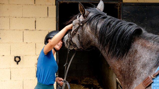 Young woman petting horse at equestrian centre stable door