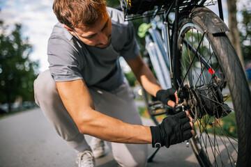 Obraz premium Young man fixes bicycle chain, concept of bike maintenance, repair, cycling, outdoor activity, urban mobility, healthy lifestyle, cycling mechanic.