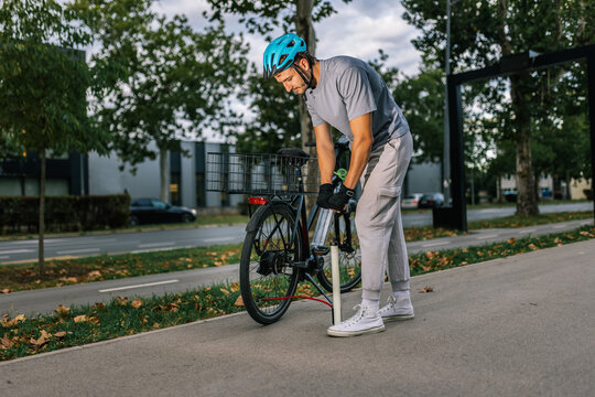 Young man inflates bicycle tire using pump, concept of bike maintenance, outdoor activity, urban mobility