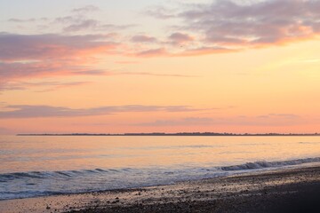A gentle sea sunset with a golden, pink sky and reflections on the water. A calm sea and a rocky beach. An atmosphere of bliss and harmony. A natural landscape for illustrations about travel, relaxati