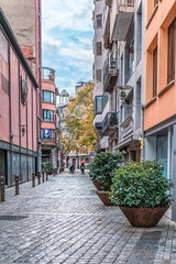 Fototapeta premium Carrer Anselm Clave street in Girona with Christmas decorations and cobblestone pavement. Modern urban scene with potted plants, pink building facades and pedestrians. Girona, Spain - November 27,2021