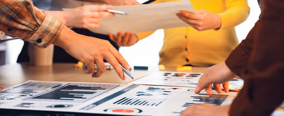 A diverse group of professionals engaged in a collaborative meeting, actively discussing and analyzing charts and data on a table, highlighting team effort and strategy. SACTR