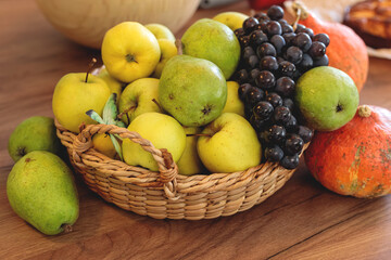 Wicker basket overflowing with a vibrant autumn harvest of yellow and green apples, dark grapes, and pumpkins on a rustic wooden table. autumn season,  autumn concept,  fall