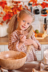 little girl baking cookies.  Cute little girl posing with a freshly baked autumn-themed cookie in her hand in a rustic kitchen while baking, featuring fall decorations. autumn season,  autumn concept