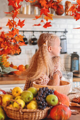 autumn still life. Happy little girl playing with dough and baking a pie in a rustic kitchen full of autumn harvest decorations, including pumpkins, fruit, and fall leaves. autumn season.