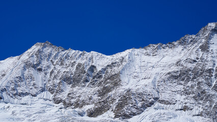 Majestic snow-covered mountain peaks rise against a clear blue sky, showcasing the beauty of nature's rugged terrain and the tranquility of high-altitude landscapes