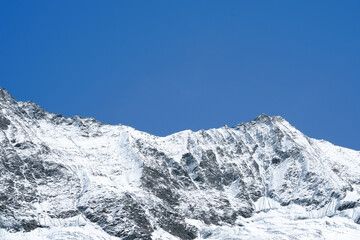 Majestic snow-covered mountain peaks rise against a clear blue sky, showcasing the beauty of nature and the grandeur of the alpine landscape in a serene environment