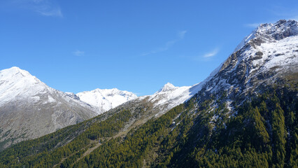 Fototapeta premium Majestic snow-capped mountains rise against a clear blue sky, showcasing rugged terrain and lush green forests, creating a breathtaking natural landscape scene