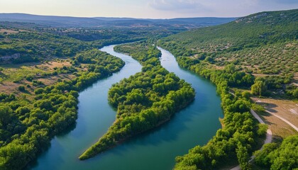 Obraz premium The image shows a river winding its way through a valley, surrounded by dense green vegetation and hills in the background.