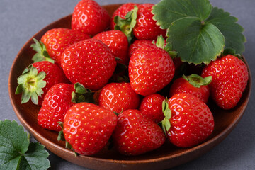 Freshly picked strawberries arranged neatly on a brown wooden plate with green leaves nearby