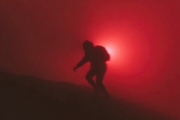 Silhouette of climber against eerie red light in foggy atmospher
