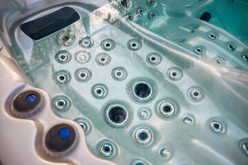 Interior of a modern hot tub featuring symmetrical jet nozzles, clear water reflecting trees,...