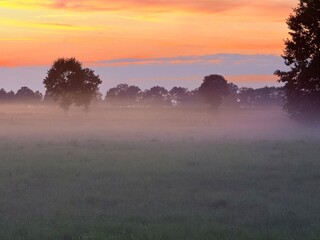 fantastic orange and purple sky, foggy sunset at the field in the countryside