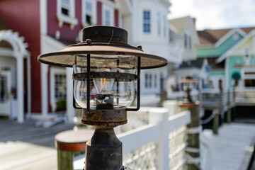 Older tungsten lamp on a fence post on a Cape Cod Beach in front of bokeh blurred colorful buildings