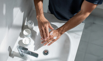 Man applying cream on hands in a bright modern bathroom. Beauty and self-care minimalistic design concept