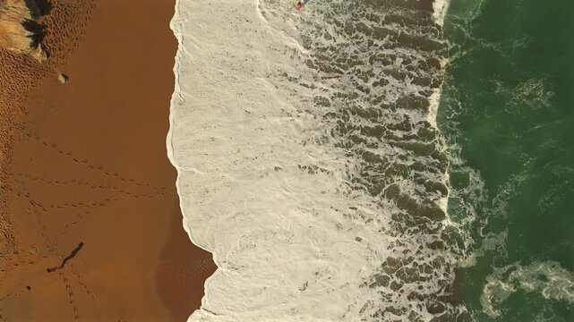Top view of sandy beach with waves and people relaxing on shore 