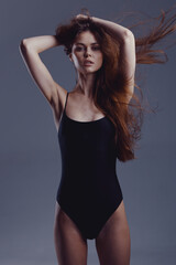 Fototapeta premium Young woman with flowing hair posing in black swimsuit with confident expression against dark background