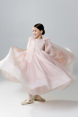 A young girl in a flowing pink dress twirls joyfully against a plain background.