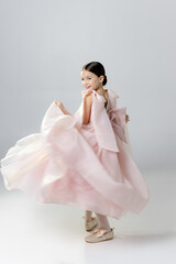 A young girl in a flowing pink dress twirls joyfully against a plain background.