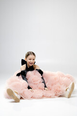 A young girl in a fluffy pink dress with black gloves poses playfully against a plain background.